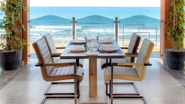 Панорамный вид на ресторан у моря с сервированным столом и видом на пляж Коста-Бланки